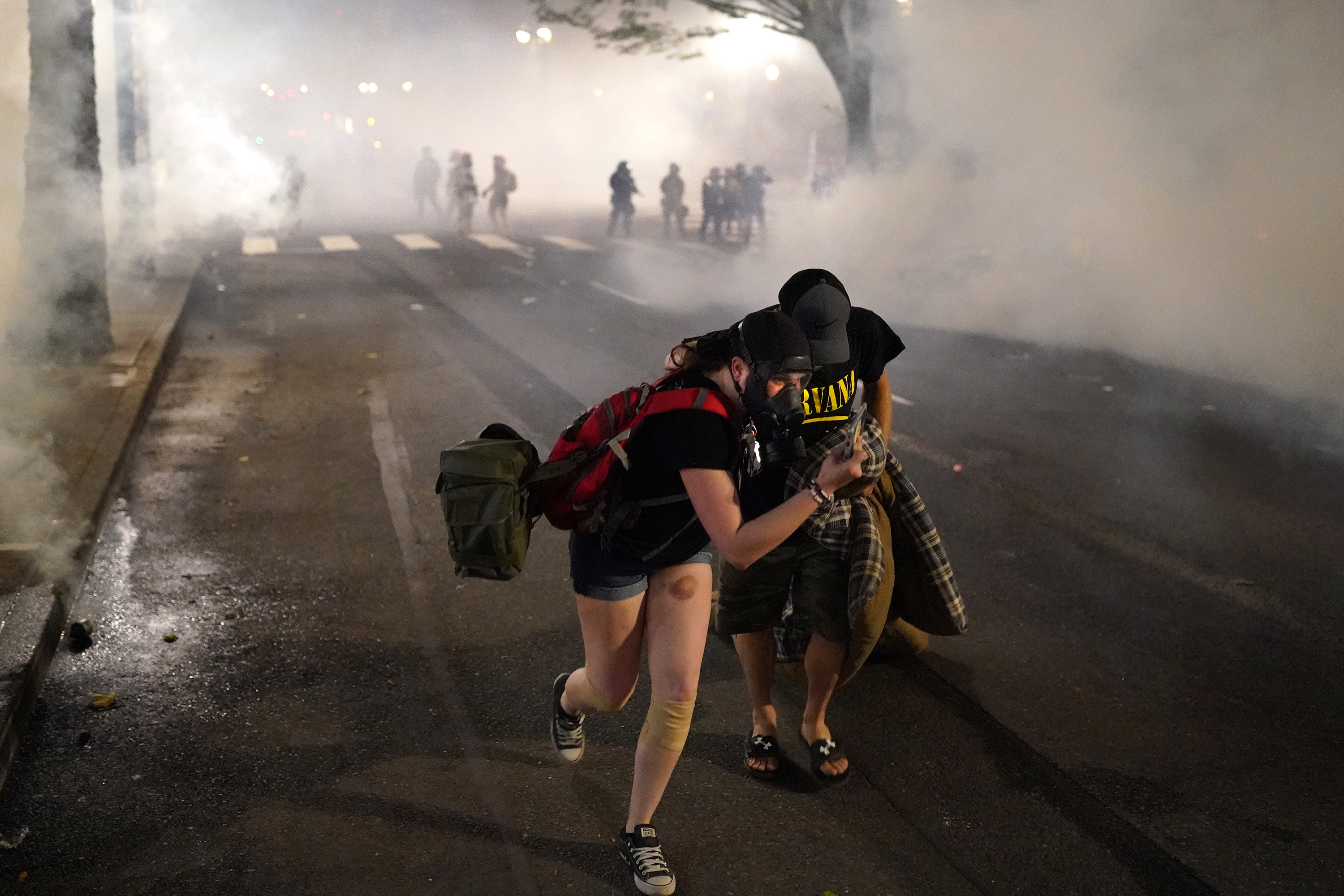 Two protesters flee through tear gas after federal officers dispersed a crowd using tear gas in Portland