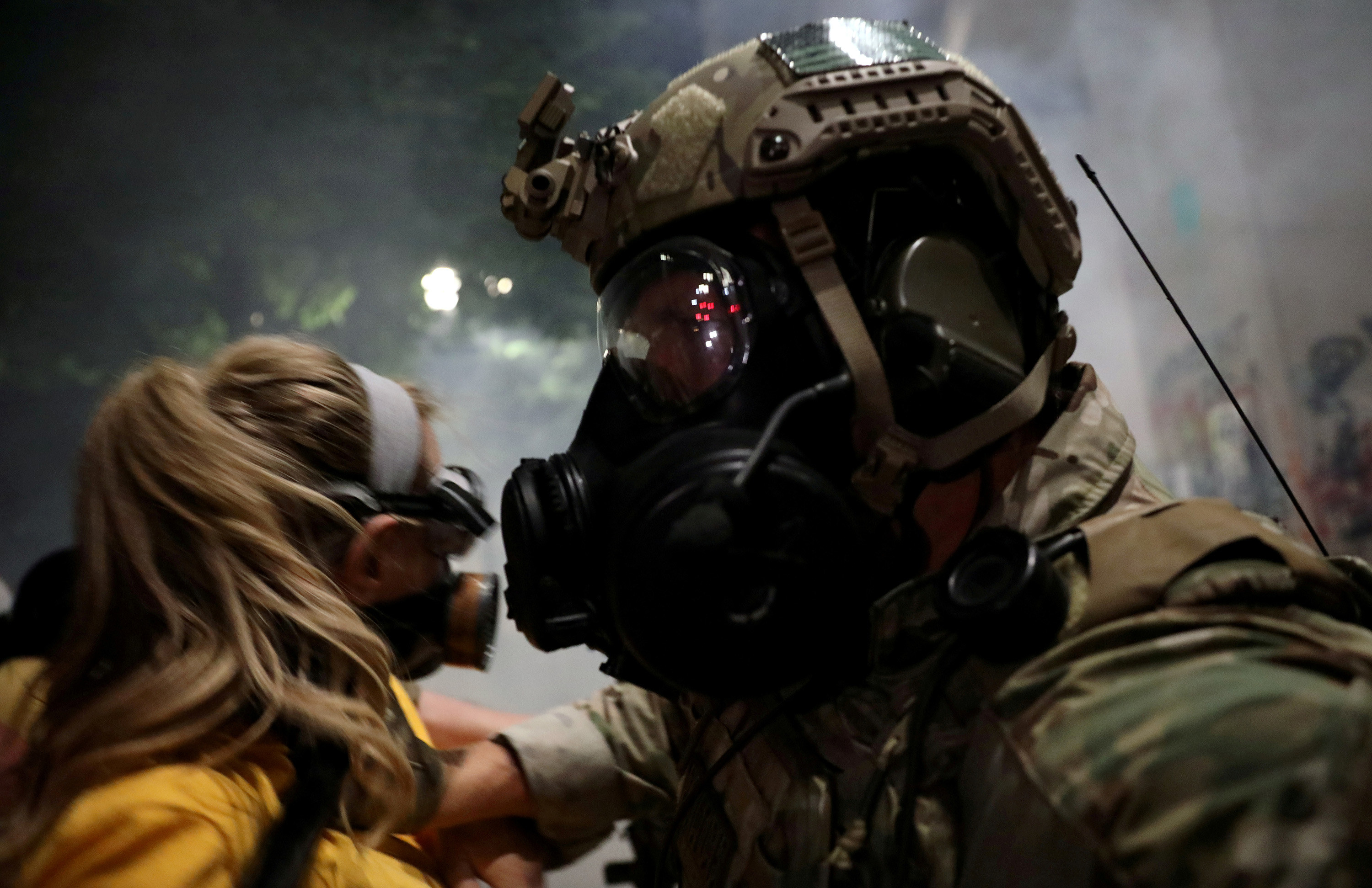 A woman in a yellow shirt and face mask faces off with a federal law enforcement officer, who pushes her back