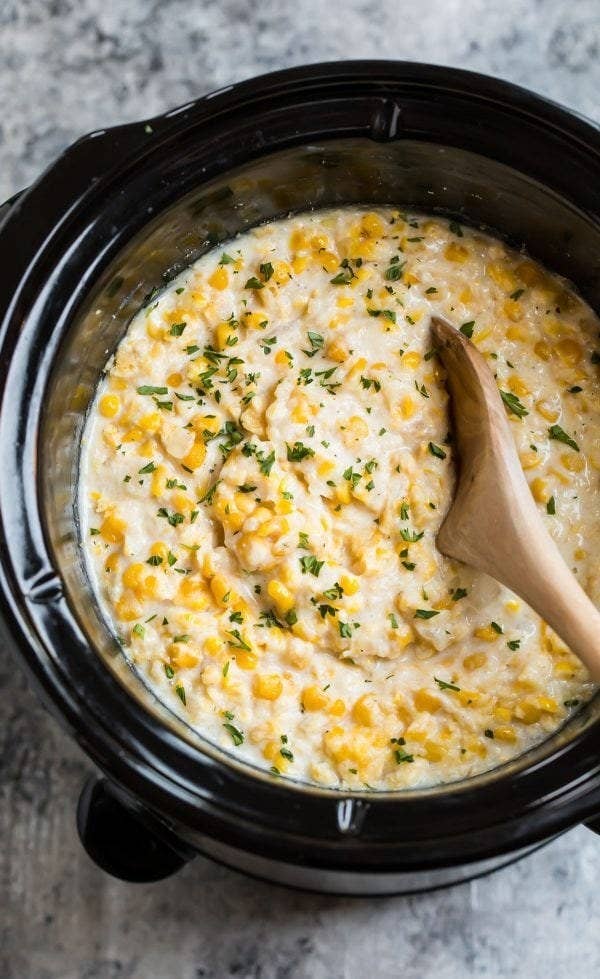A slow cooker filled with creamy corn and fresh herbs.