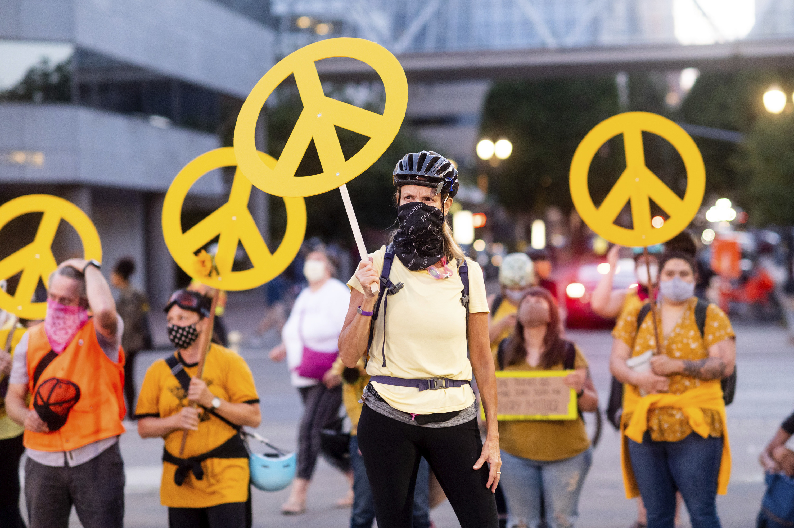 A woman holds a yellow peace sign with others in the crowd wearing matching yellow shirts doing the same during a protest