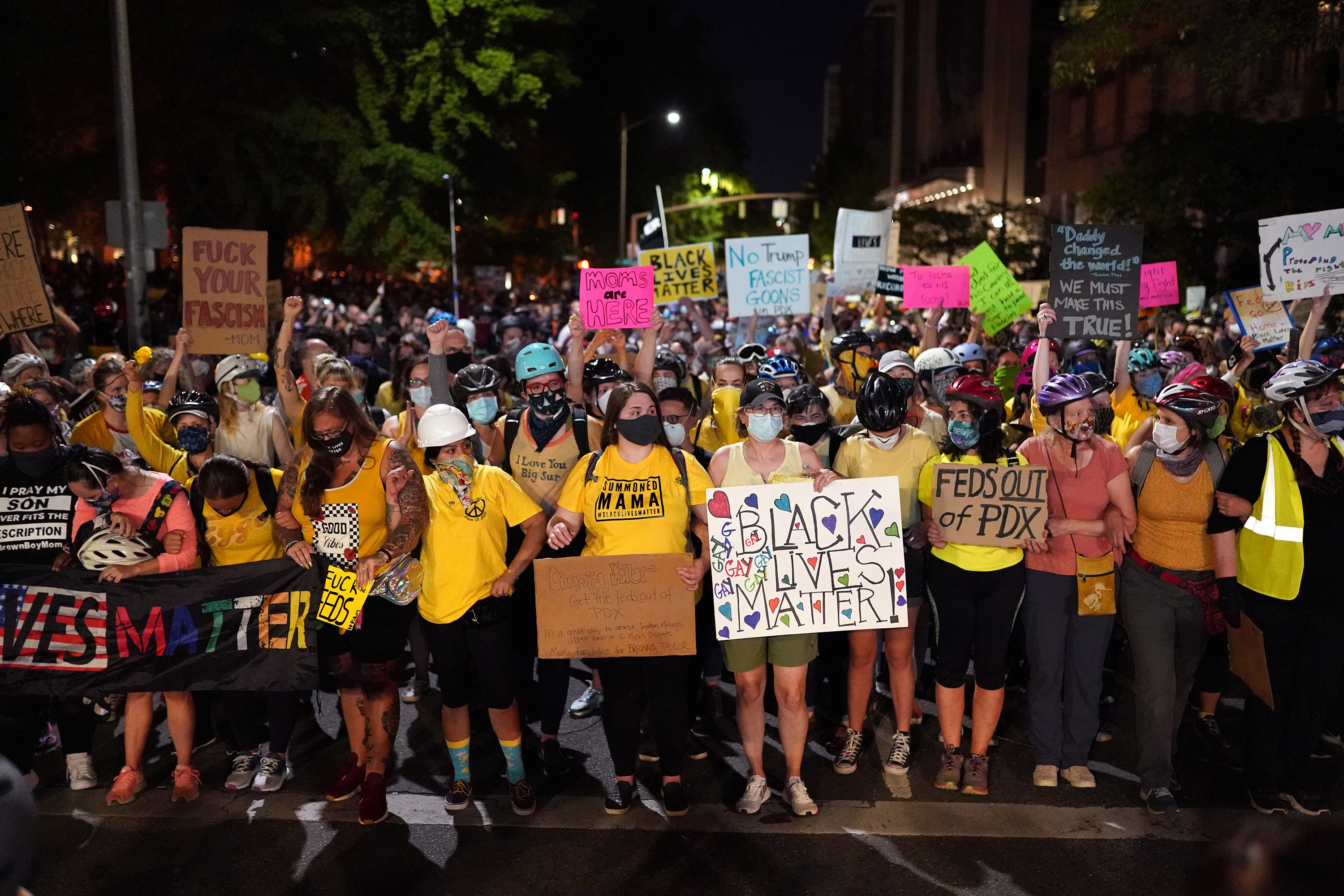 Dozens of mothers in yellow shirts form a front line in a protest march in Portland. They hold signs reading &quot;Black Lives Matter,&quot; &quot;Feds out of PDX,&quot; and &quot;Moms are here.&quot;