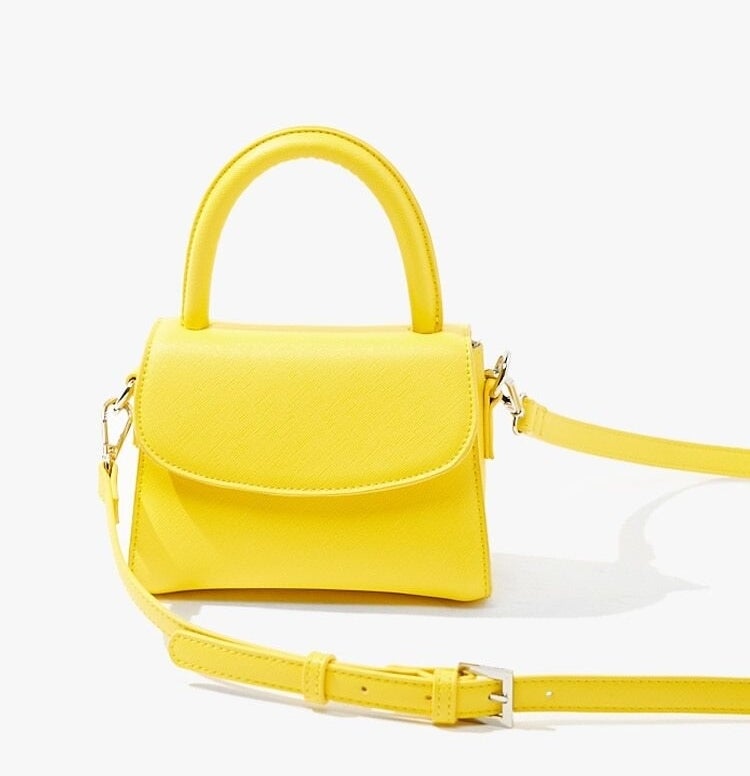 A tiny, bright yellow purse with a flap closure, large structured handle, and metal buckle details on the long strap