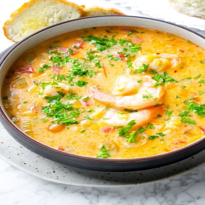 A bowl of creamy seafood soup with crab meat, shrimp, and lots of fresh chopped herbs.