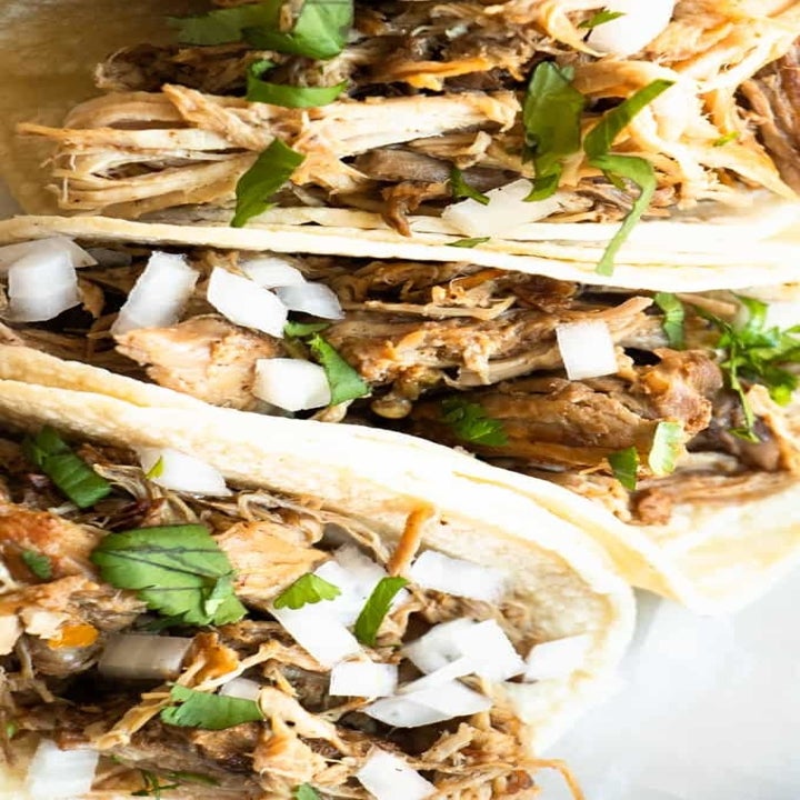 Three tacos filled with shredded pork carnitas, onion, and cilantro.