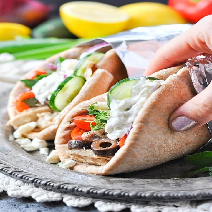 A hand grabbing a pita filled with chicken gyro and shredded veggies with yogurt sauce.