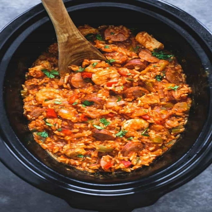 A slow cooker filled with jambalaya: rice with sausage, shrimp, chicken, and veggies.