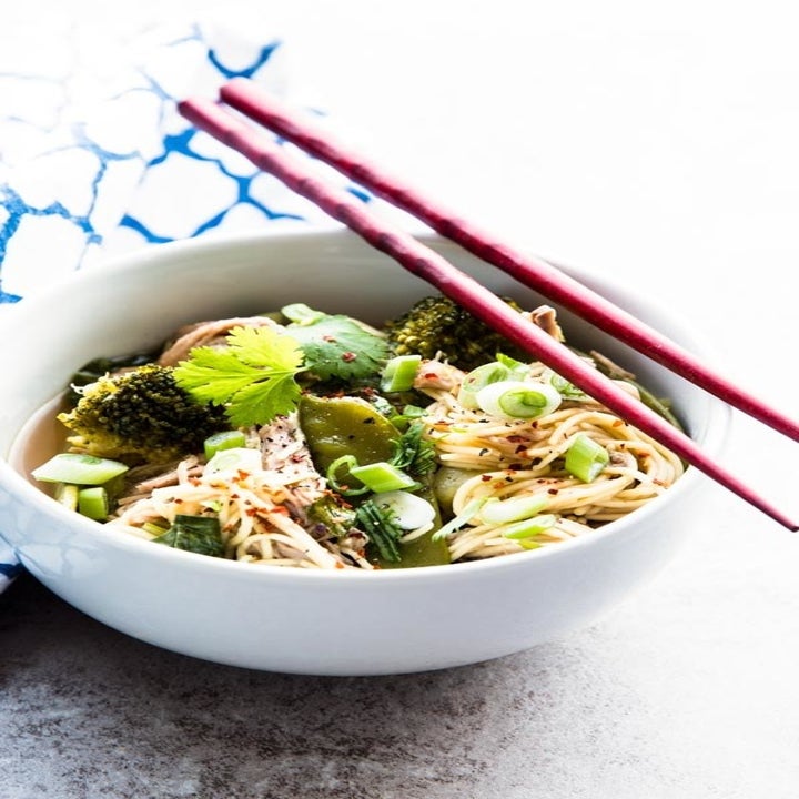 A bowl of shredded pork and noodles with green veggies.
