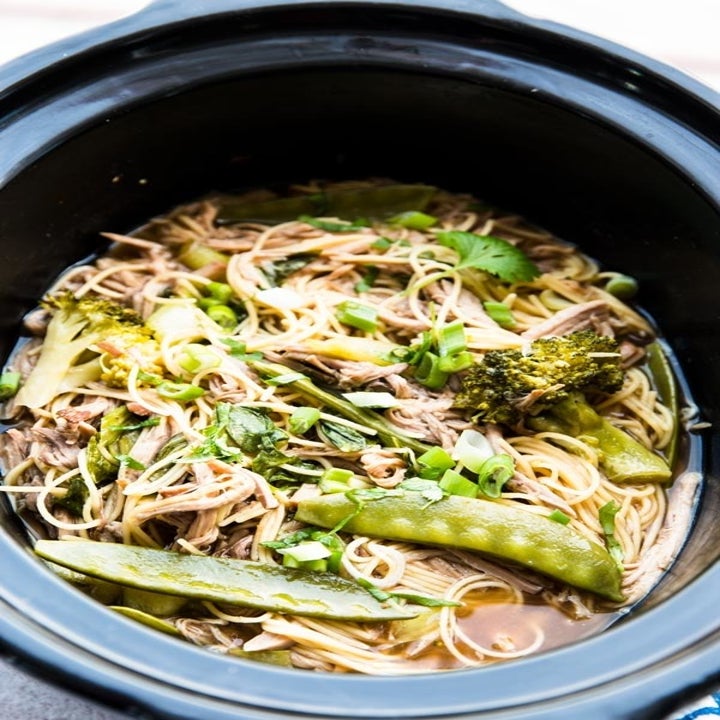 A slow cooker with noodles, shredded pork, broccoli and snap peas.