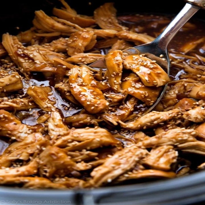 A slow cooker full of shredded chicken in a honey teriyaki sauce with sesame seeds.