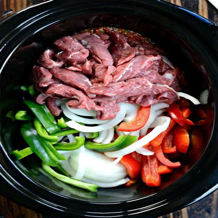 Sliced steak, onions, and peppers in a slow cooker to make fajitas.