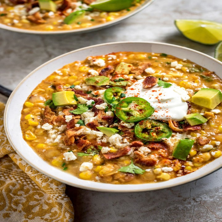 A bowl of Mexican street corn soup that has been garnished with cheese, bacon, Jalapeño, and avocado.