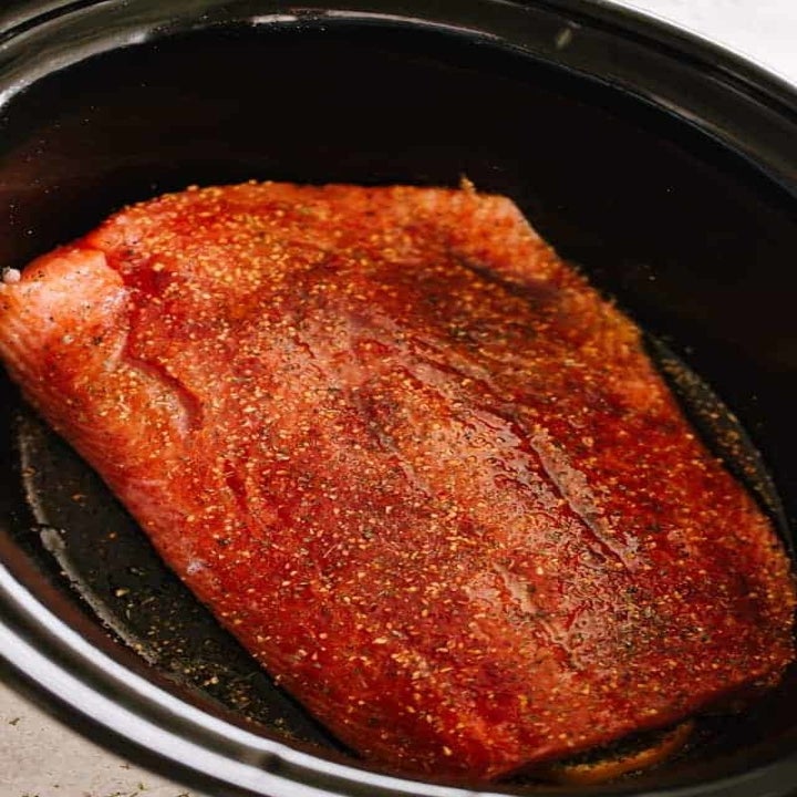 Raw salmon rubbed with oil and spices in a slow cooker.