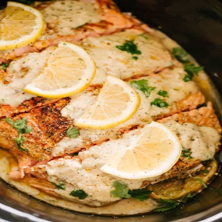 Four slices of salmon topped with creamy sauce and lemon slices.