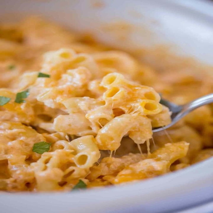 A spoon digging into a slow cooker full of creamy mac 'n' cheese.