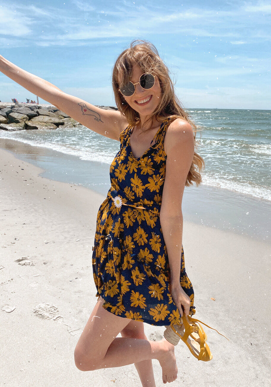 Model wearing the navy-and-yellow floral midi dress, featuring tied shoulder straps and a ruffle along its hem