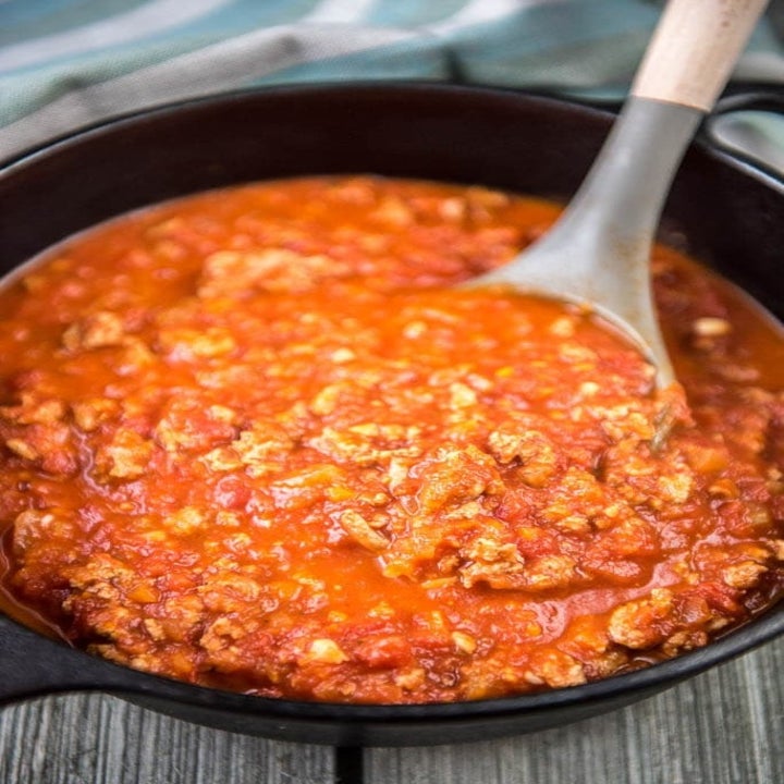 A wooden spoon stirring a pot of turkey Bolognese sauce.