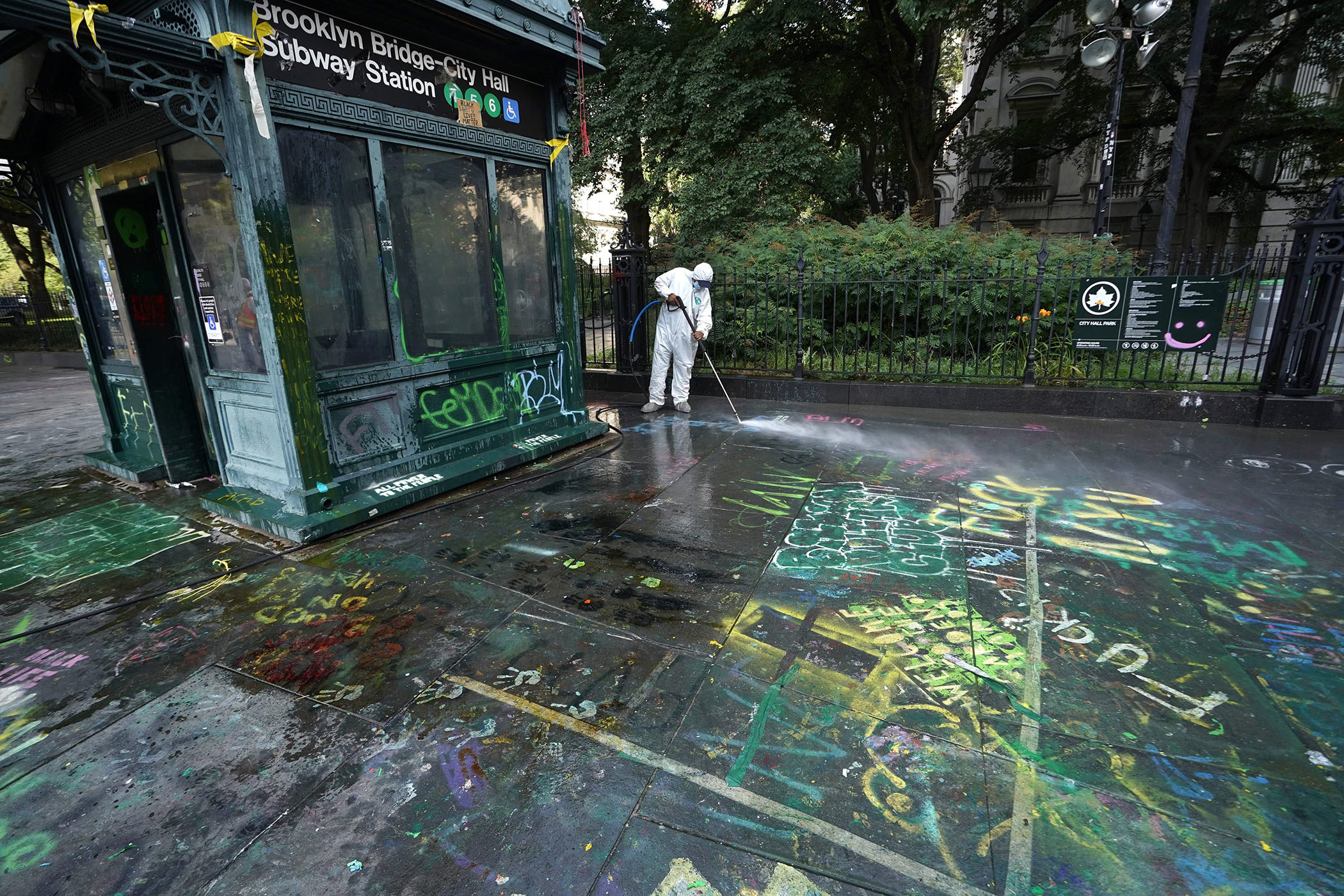 A sanitation worker dressed in an all-white uniform washes graffiti on the ground outside the Brooklyn Bridge–City Hall Subway Station