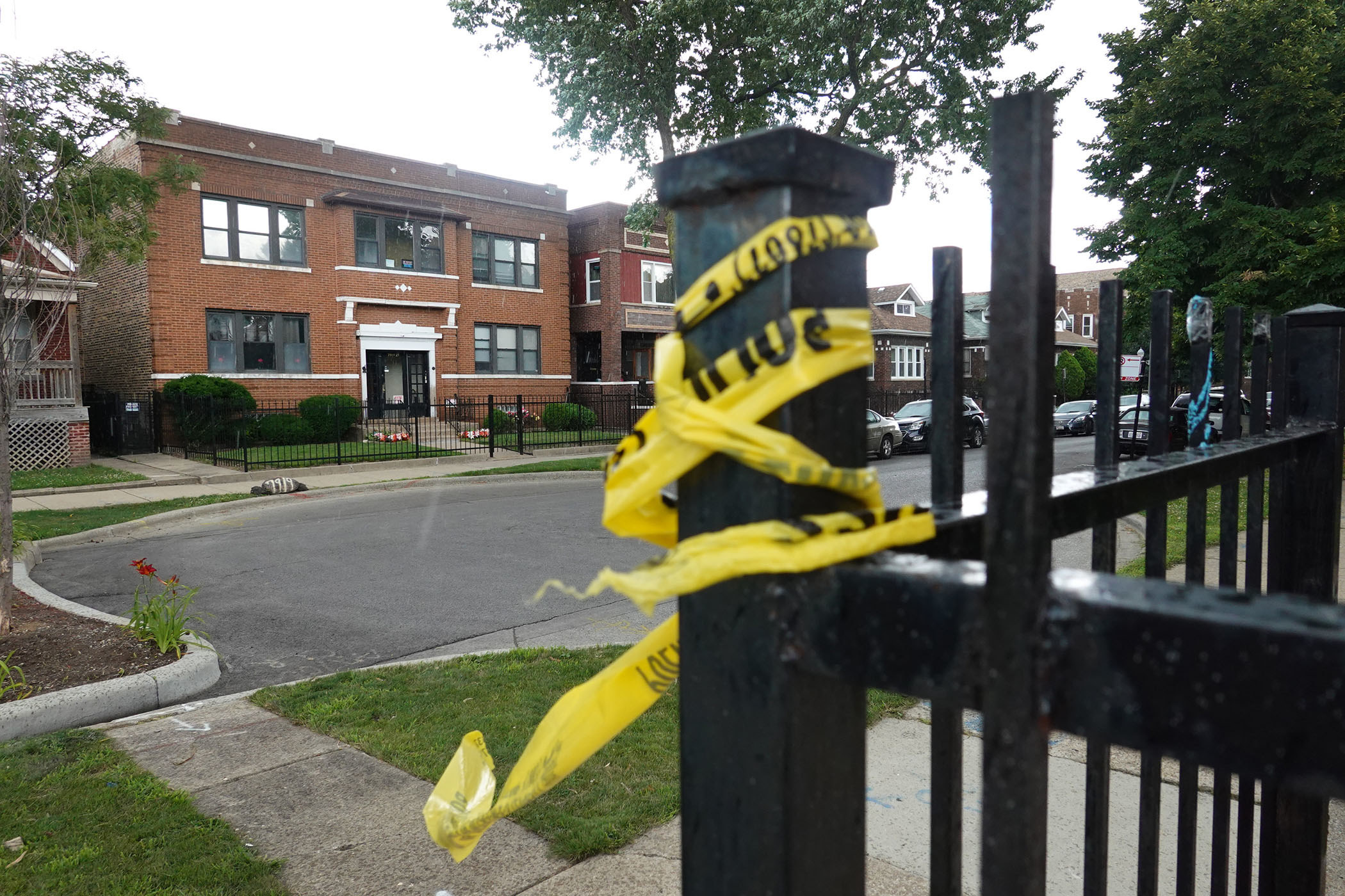 Yellow caution tape is wrapped around an iron fence; in the background, an empty street and brick buildings