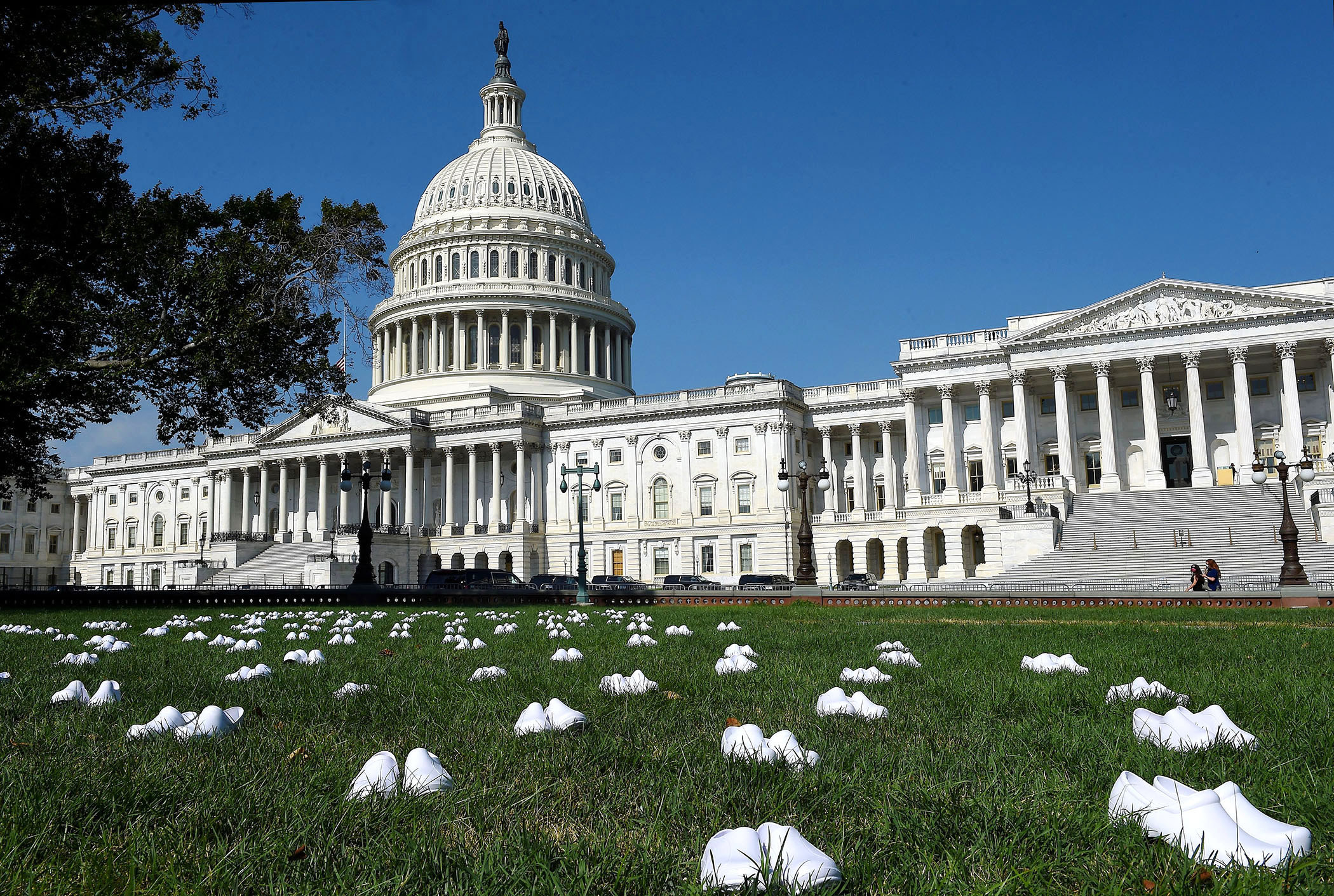Several pairs of white clogs sit on the lawn outside the US Capitol building
