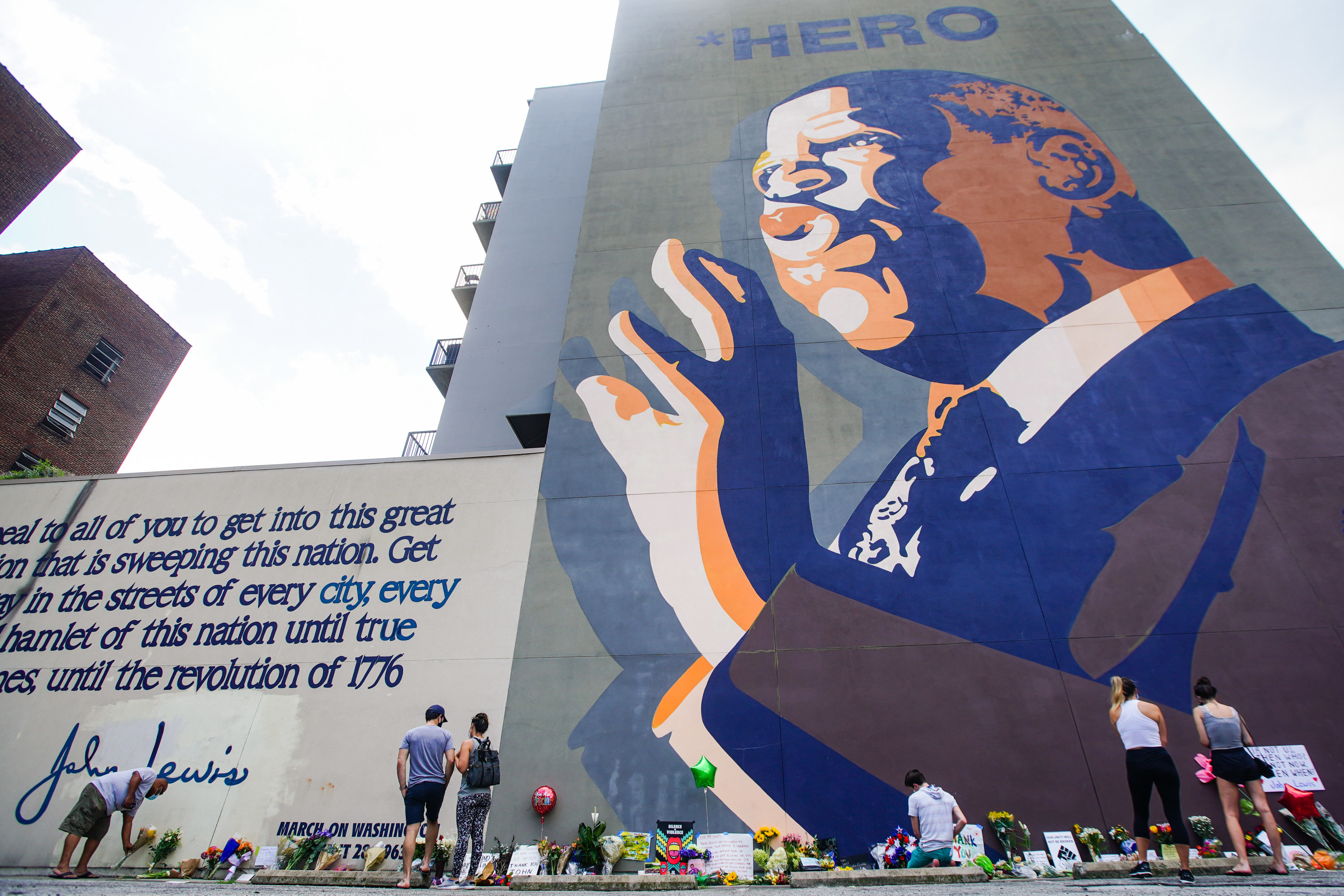 People leave flowers, balloons, and cards, on the ground beneath a towering mural of Rep. John Lewis that says the word &quot;Hero&quot; at the top