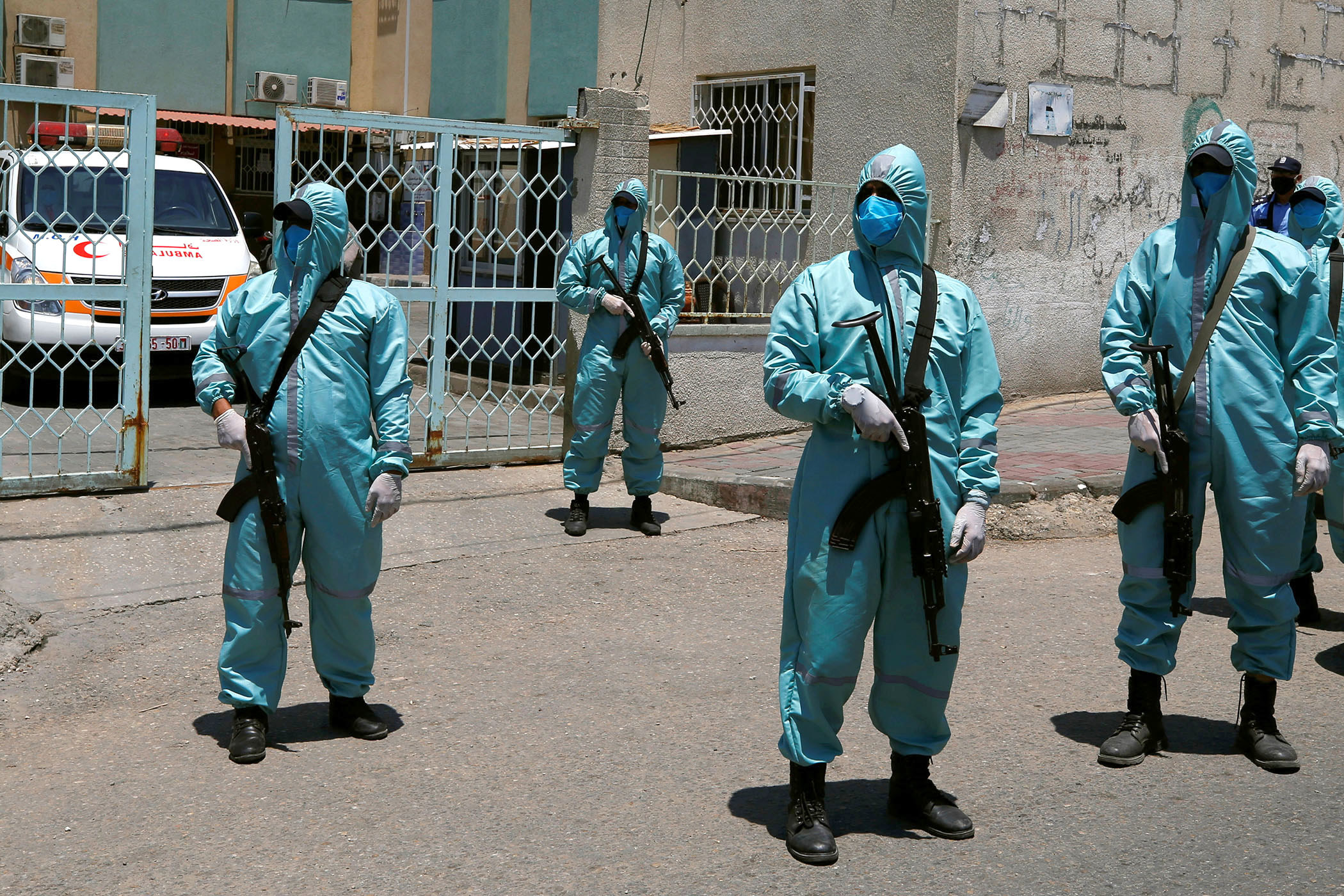 Five people in full-body protective gear, face masks, and black boots, stand with automatic weapons on the street