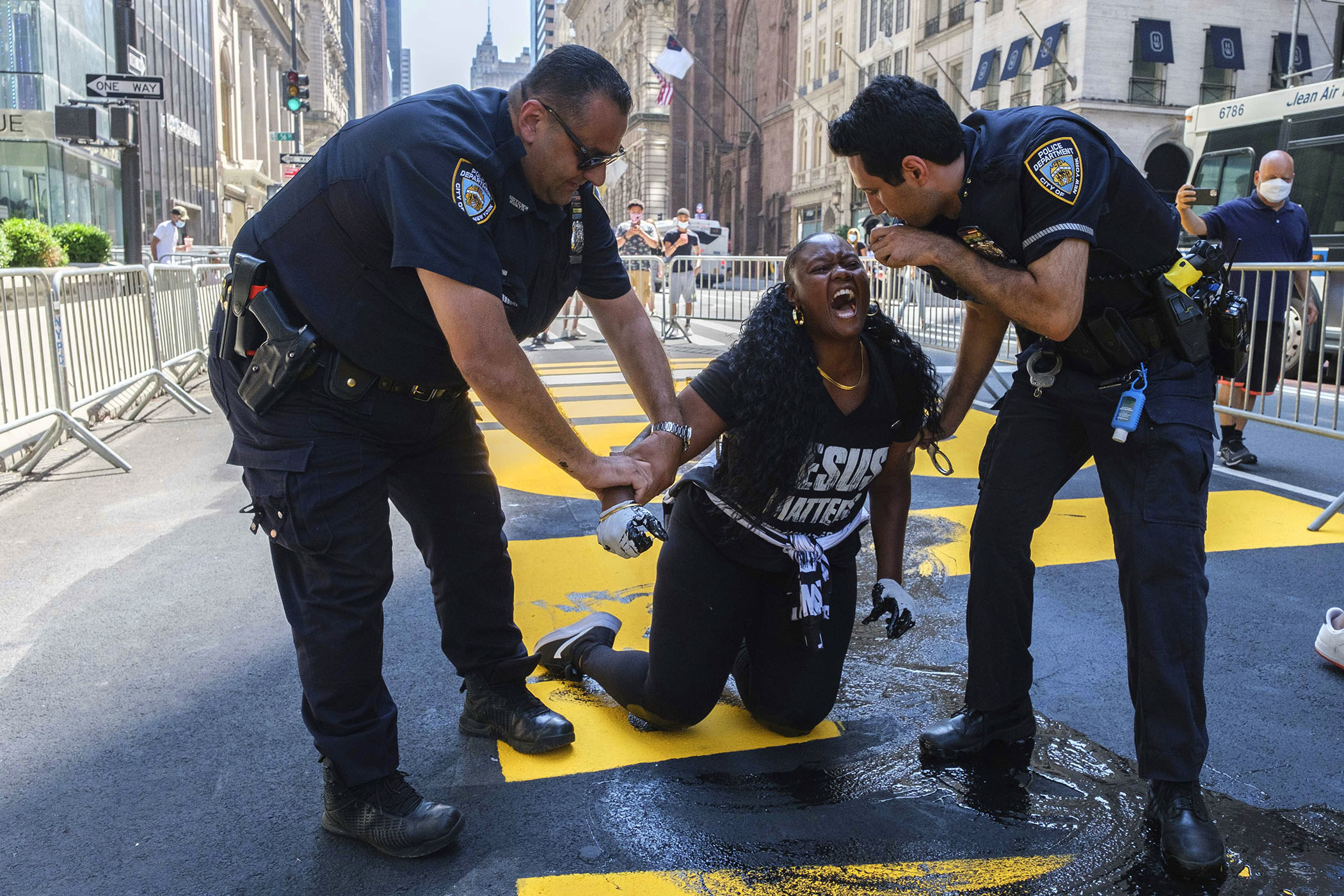 Two police officers hold onto the arms of a screaming woman kneeling on the ground