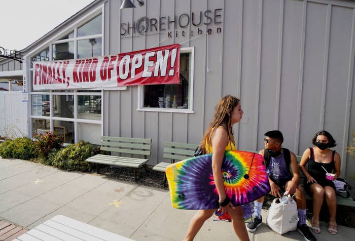 Two people sit and wait outside a restaurant that displays a banner that reads "Finally, kind of open!"