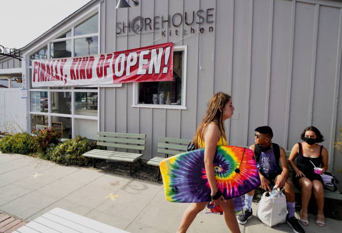 Two people sit and wait outside a restaurant that displays a banner that reads &quot;Finally, kind of open!&quot;