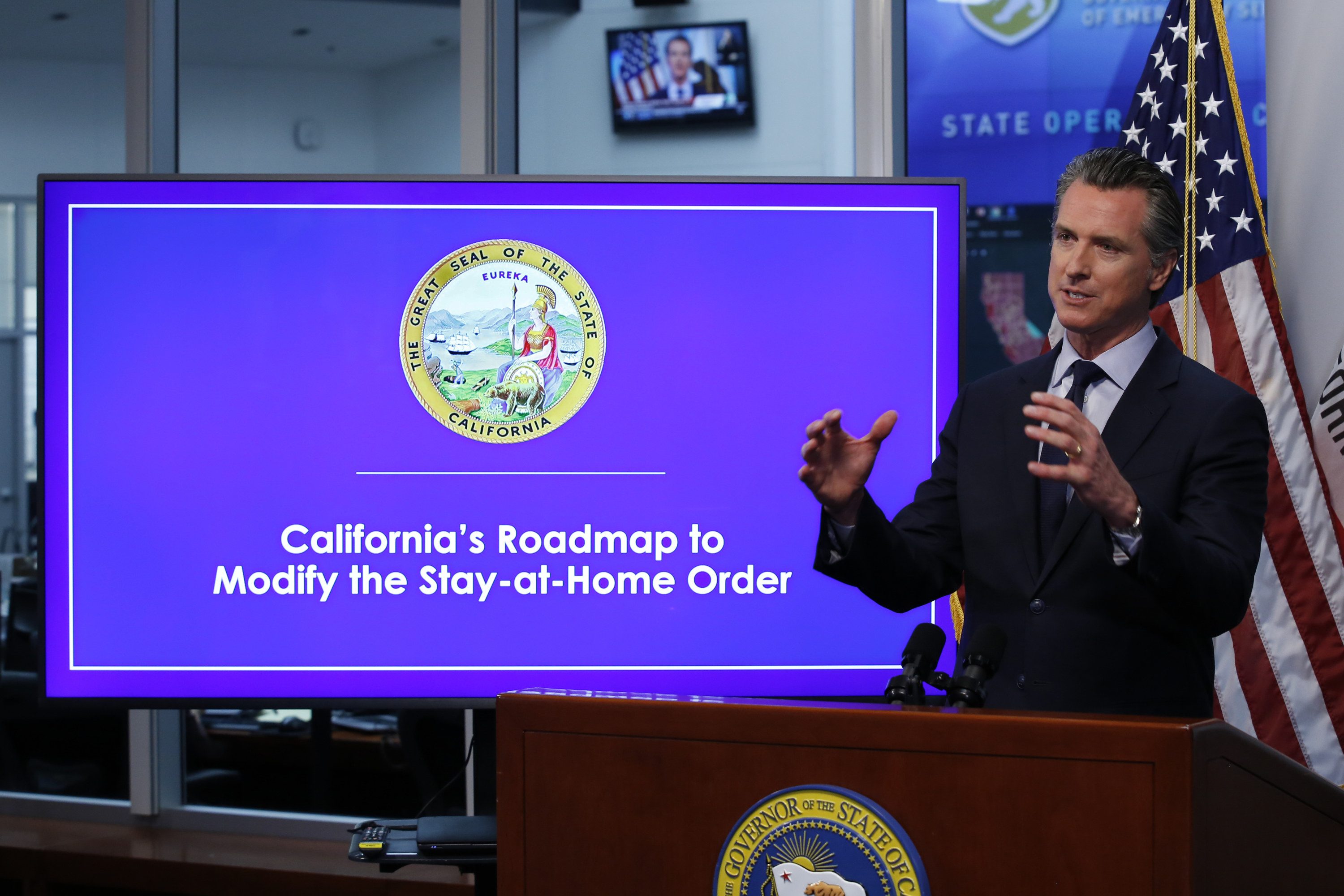 Gavin Newsom, governor of California, stands behind a lectern and gives a speech in front of a large monitor that reads &quot;California&#x27;s Roadmap to Modify the Stay-at-Home order&quot;