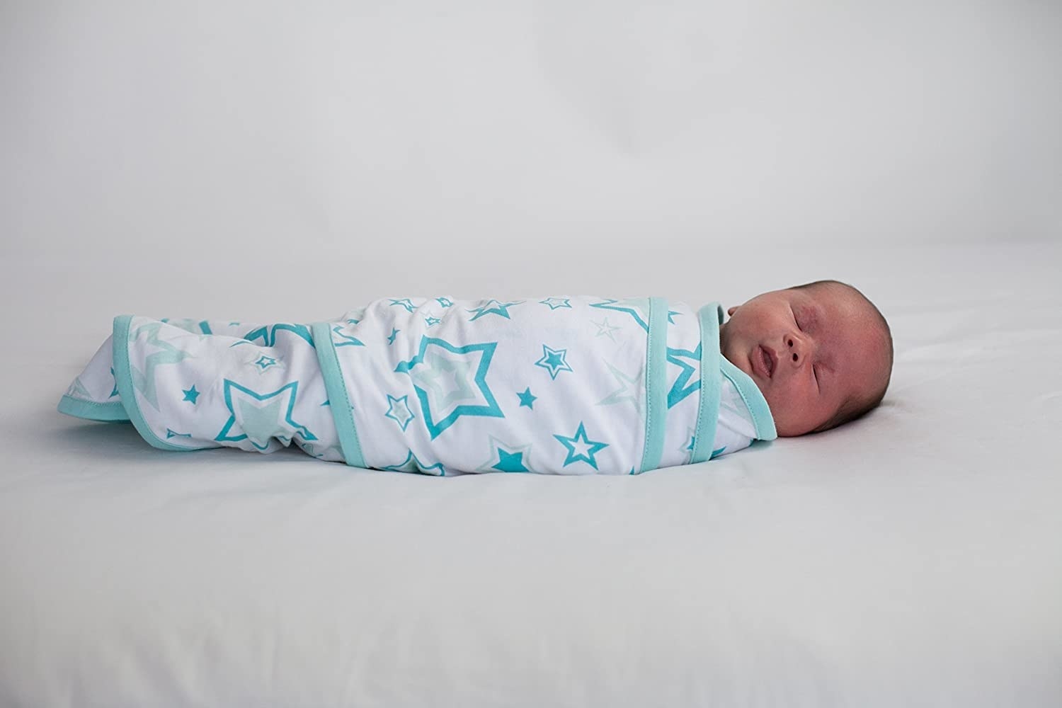 A baby model swaddled in a white wrap with teal accents and stars