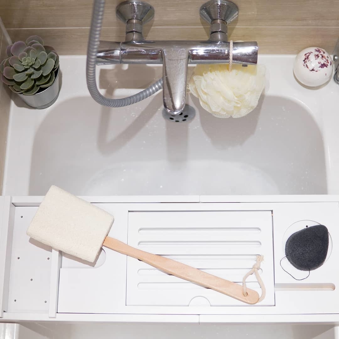 A loofah sponge attached to a long wooden handle sitting on a bath tray