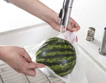 Model's hand's holding a small watermelon in bamboo towel under running water