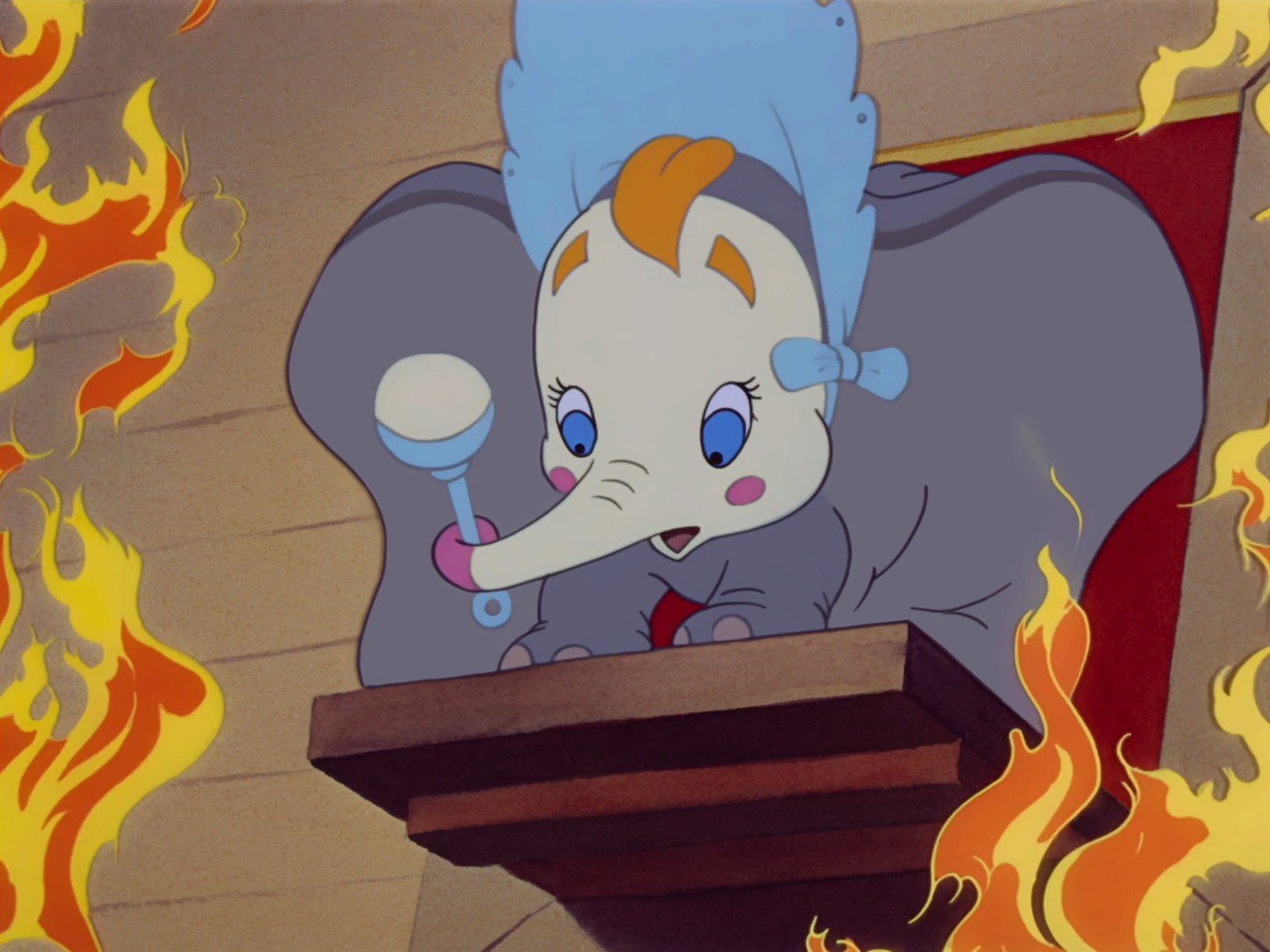 Dumbo, who&#x27;s dressed like a baby, stands on a plank in the middle of flames