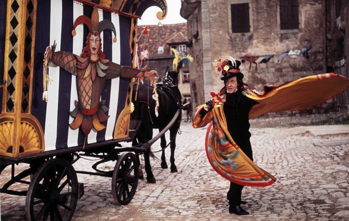 The Child Catcher, a man with a carnival hat and cloak, stands outside his horse and carriage