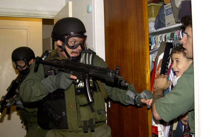 An armed federal agent points an automatic rifle at a young boy