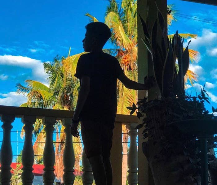 A teenager, standing on a patio, faces away from the camera