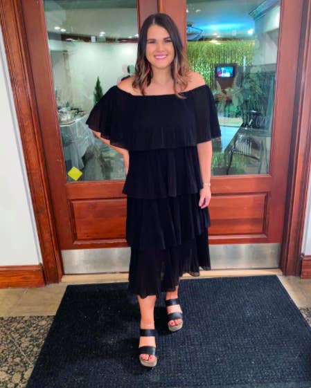 reviewer wearing a black multi-tier pleated dress with off the shoulder structure