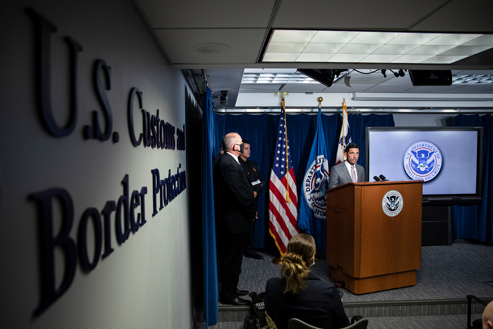 Men stand on a stage in a press briefing room