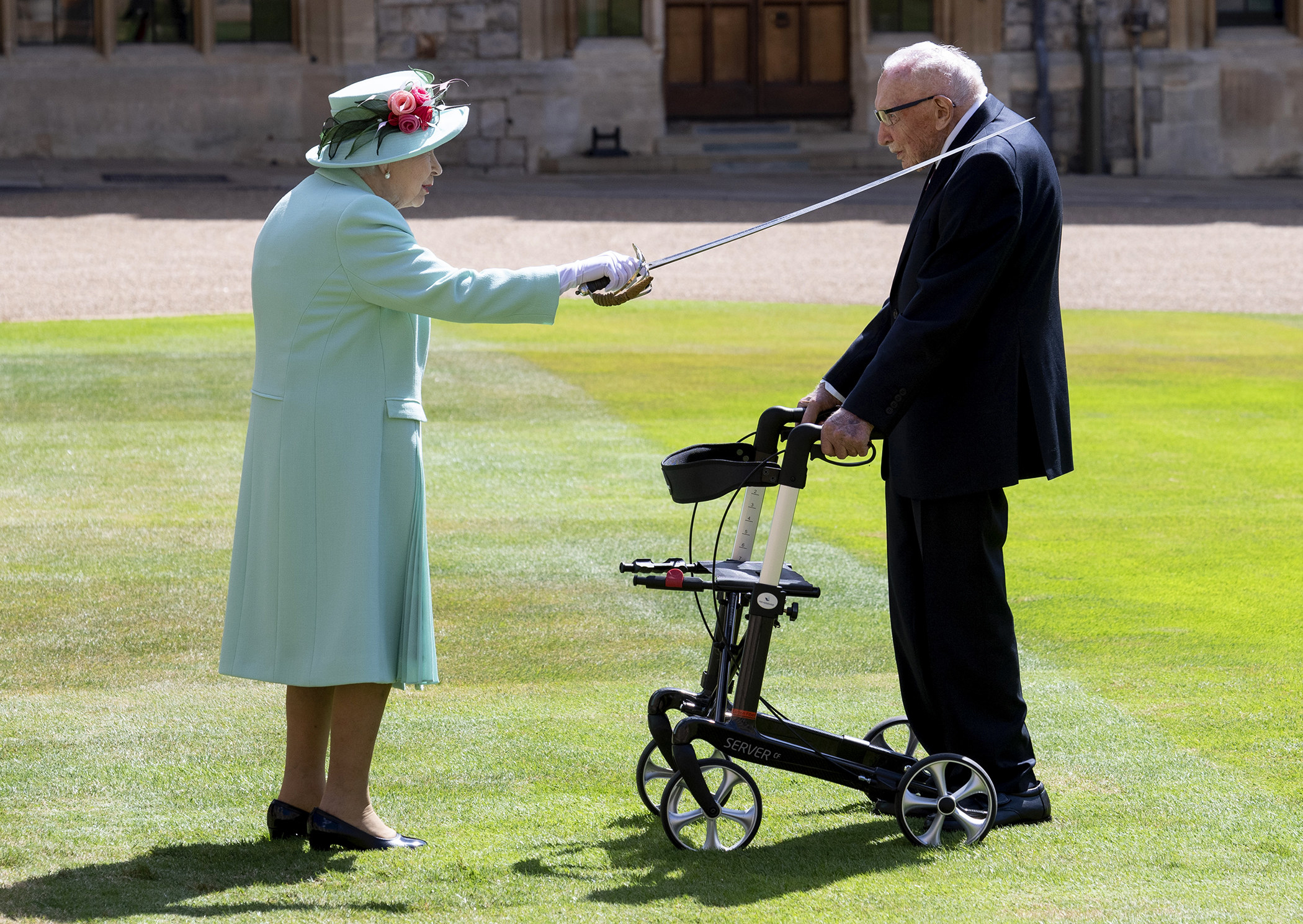 The Queen (left) uses a sword to tap the left shoulder of Sir Thomas Moore (right) as both stand on the grass