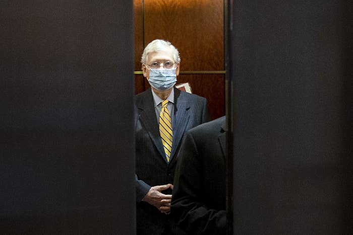 Mitch McConnell, wearing a blue mask and yellow tie, stands in an elevator as the doors close in front of him