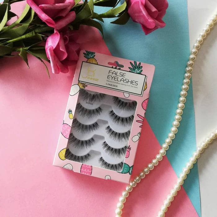 A pack of false eyelashes on a table beside a strand of peals and flowers