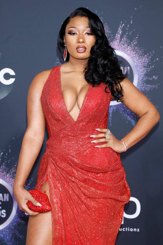 Megan Thee Stallion poses at an event wearing a sparkly red dress with a matching purse and earrings