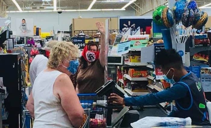 A woman wearing a swastika face covering raises her hand in the air while at a checkout. 