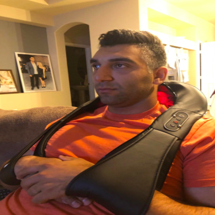 A reviewer wearing the massager around their neck, with the heated part on the back of their neck and the straps coming around the sides. Their arms are through the strap loops