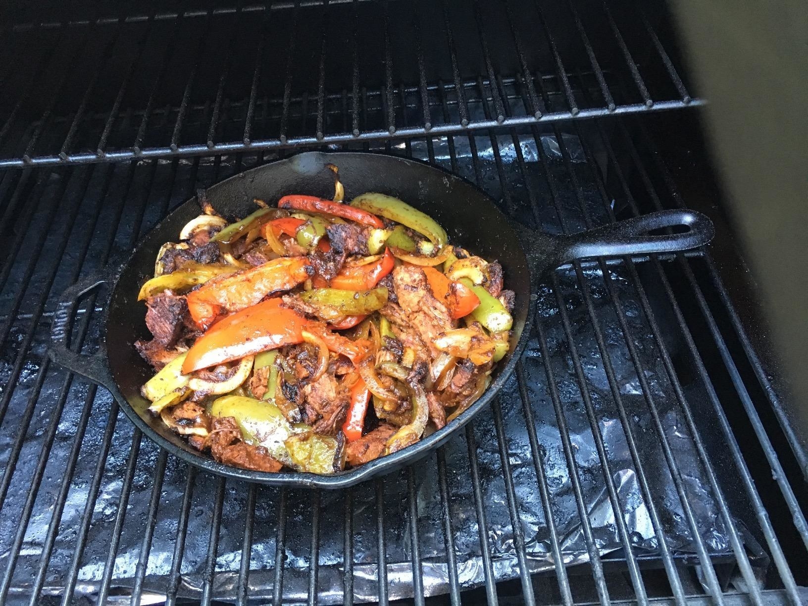 Chicken and pepper cooking in a cast iron skillet on the grill.