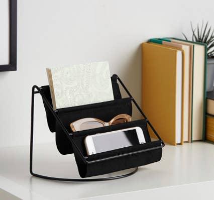 The hammock organizer on a desk filled with a phone sunglasses and a notebook