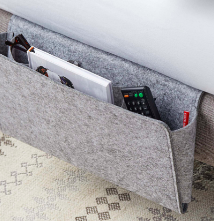 The storage caddy packed with a remote control glasses and a notebook and tucked under a mattress