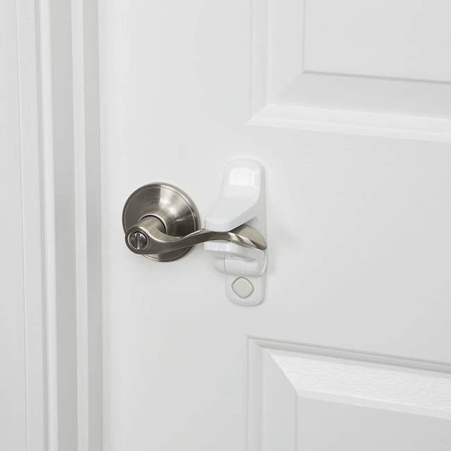 A lever door handle being held in place with a white lock. The lock is placed above and below the handle and has a push-button release system. 