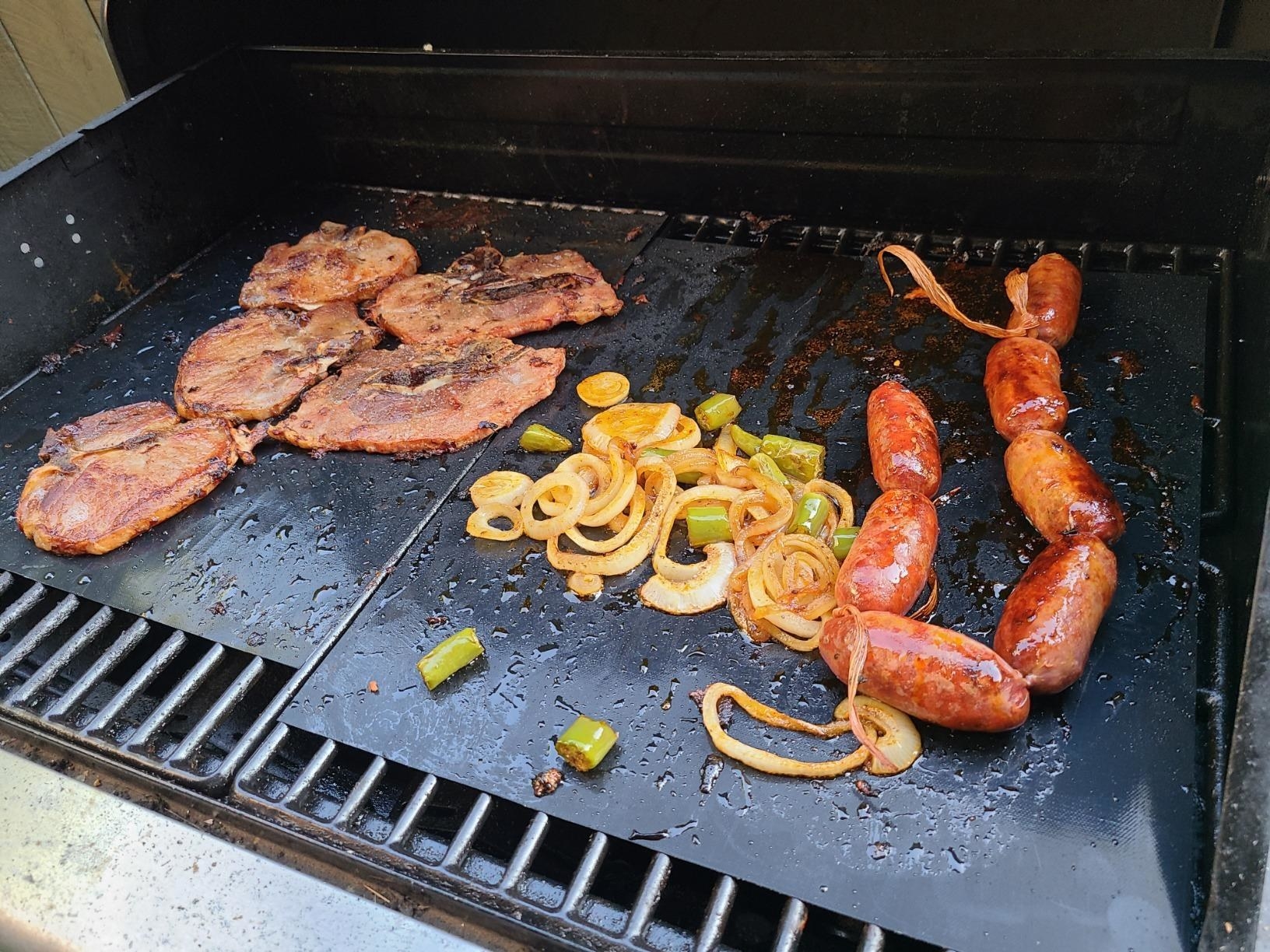 Chicken, peppers, and chorizo cooking on top of the non-stick grill mats on the grill.