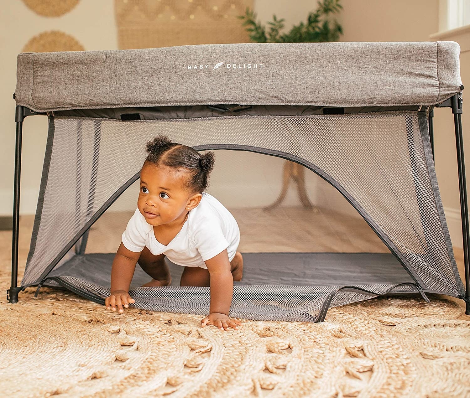 A baby crawling out of the bottom door in the mesh play space. All sides are clear mesh with a fabric cover on the top, covering the adjustable poles that create the frame